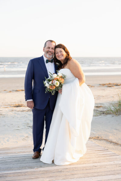 Newlyweds happily posing on a beach at sunset.
