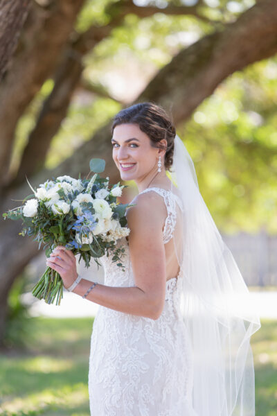 Bride in a lace wedding dress holding a bouquet outdoors.