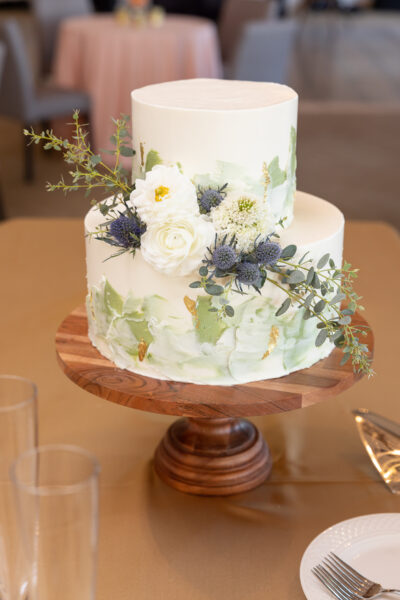 Elegant two-tier floral wedding cake with white and blue flowers.