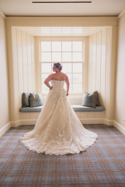 Bride in an elegant wedding gown standing by a large window.