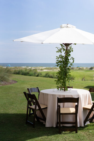 Outdoor dining setup with a round table, chairs, and umbrella by the seaside.