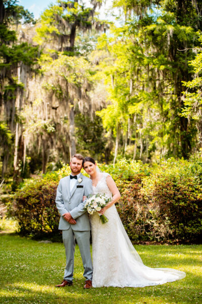 Bride and groom posing outdoors in a lush green setting.
