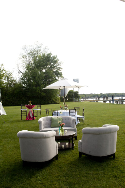 Outdoor seating area with cushioned chairs and umbrella on a lawn near water.