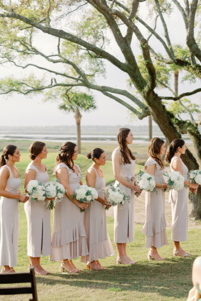 Bridesmaids in soft pink dresses holding white bouquets outdoors.