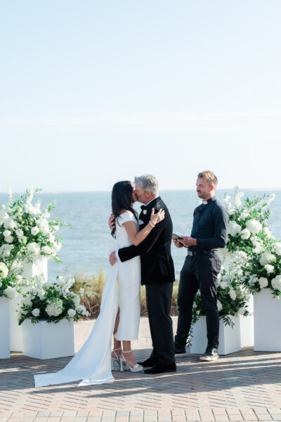 Couple sharing a romantic kiss at a seaside wedding ceremony.