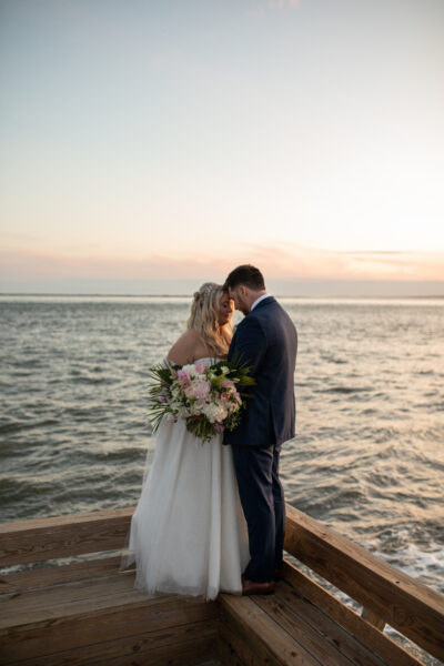 Bride and groom embracing by the water at sunset.