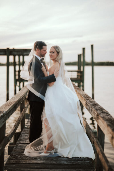 Newlyweds embrace on a rustic pier at sunset.