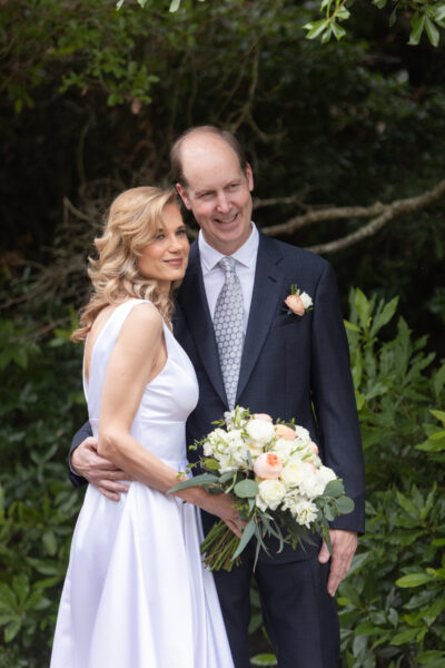 Bride and groom smiling together in a garden setting.