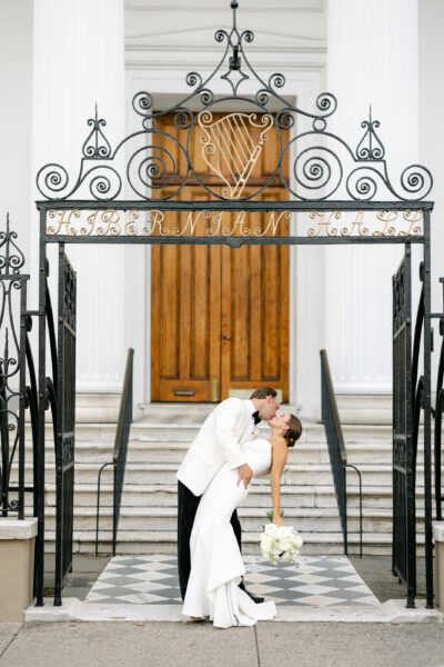 Bride and groom kissing under ornate gate in front of wooden doors.