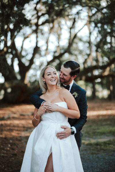 A joyful bride and groom embracing outdoors with trees in the background.