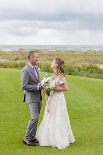 Newlyweds share a joyful moment outdoors on a grassy field.