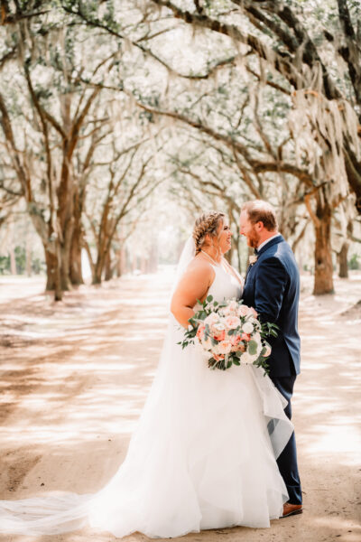Bride and groom sharing a romantic moment on a tree-lined path.