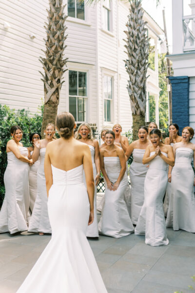 Bride in white gown with bridesmaids in matching dresses outdoors.