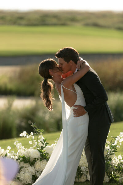 A couple shares a romantic kiss in a sunlit outdoor setting.