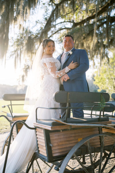 A bride and groom pose happily on a vintage carriage outdoors.