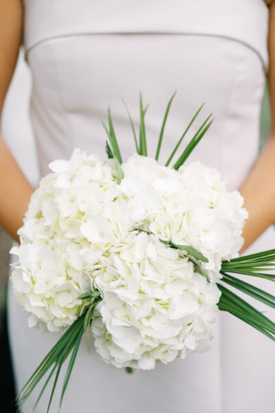 Bride holding a bouquet of white flowers with green leaves.