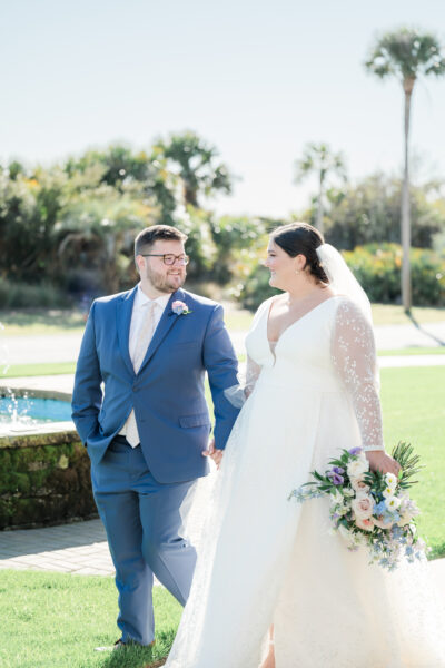 Newlywed couple walking hand in hand outdoors, smiling joyfully.