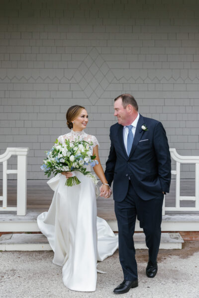 Bride and groom holding hands, smiling on wedding day.