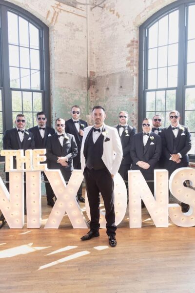 Groom and groomsmen posing with large letters spelling 'The Nixons'.