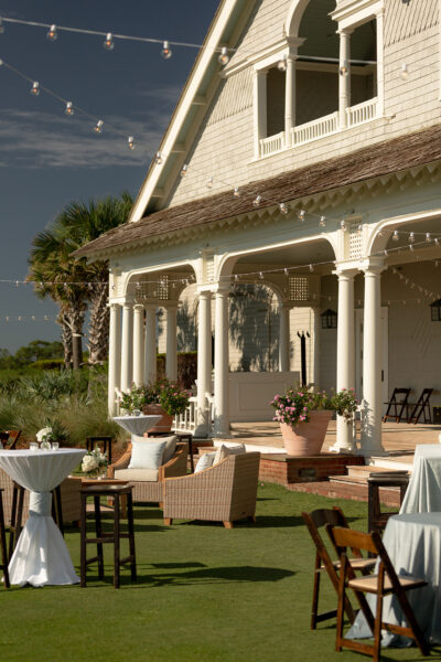 Elegant outdoor patio with wicker furniture and white tablecloths beside a charming house.