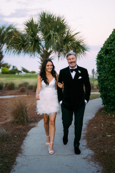 Couple walking hand-in-hand outdoors in elegant evening attire.