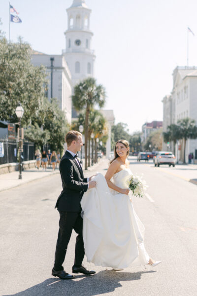 Bride and groom walking hand in hand down a sunny city street.