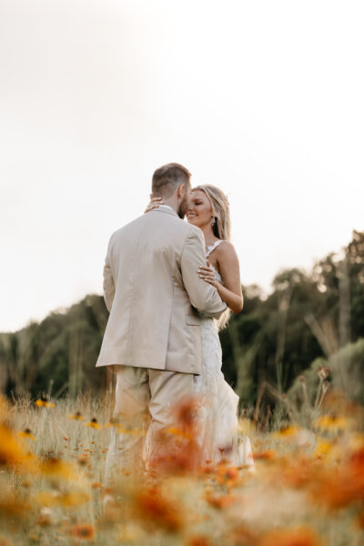 Couple embracing in a field of yellow flowers during golden hour.