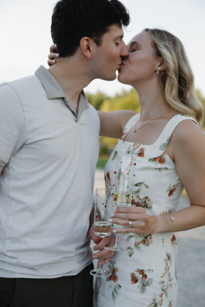 Couple sharing a kiss, holding champagne glasses outdoors.