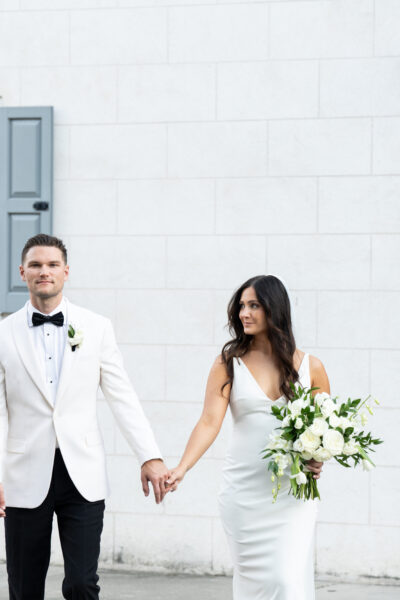 Bride and groom holding hands outdoors in elegant wedding attire.