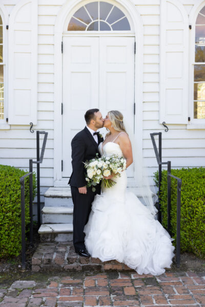 Bride and groom share a kiss on the steps of a white building.