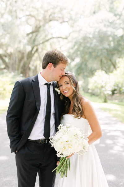 A groom kisses the bride on the forehead during their wedding day.