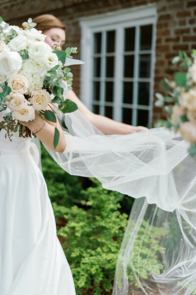 Bride holding bouquet with flowing veil outdoors.
