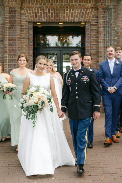 Bride and groom with their wedding party posing outside a brick building.