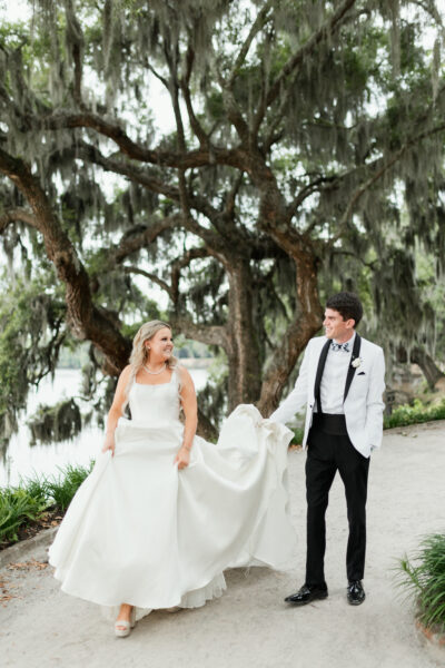 Bride and groom holding hands under mossy trees on wedding day.