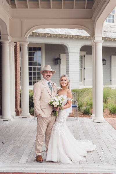 Bride and groom posing outside a charming venue, smiling happily.