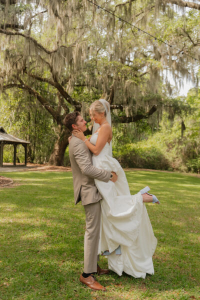 Groom lifting bride in a joyful outdoor wedding moment.