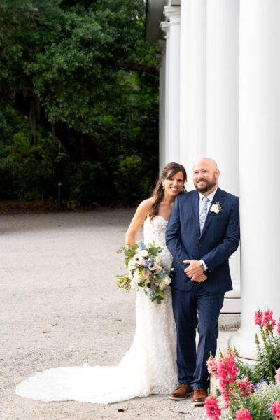 Bride and groom posing outdoors beside white columns.