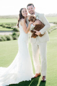 Newlyweds holding a small dog during outdoor wedding photos.