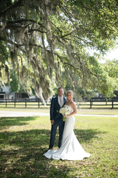 Bride and groom standing under a large tree on their wedding day.