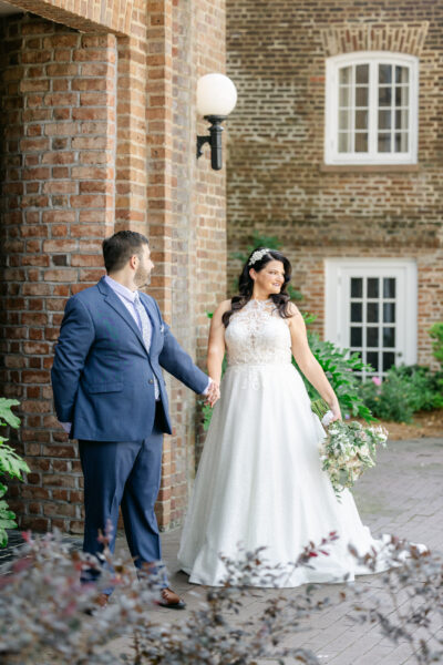 Bride and groom holding hands outside a historic brick building.