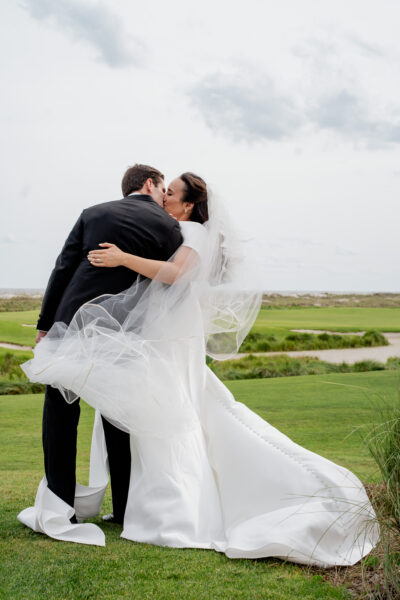Newlyweds share a joyful kiss outdoors on their wedding day.
