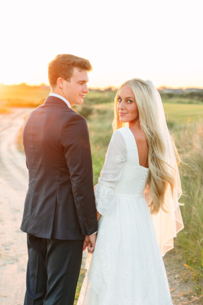 Couple holding hands outdoors at sunset, dressed formally.